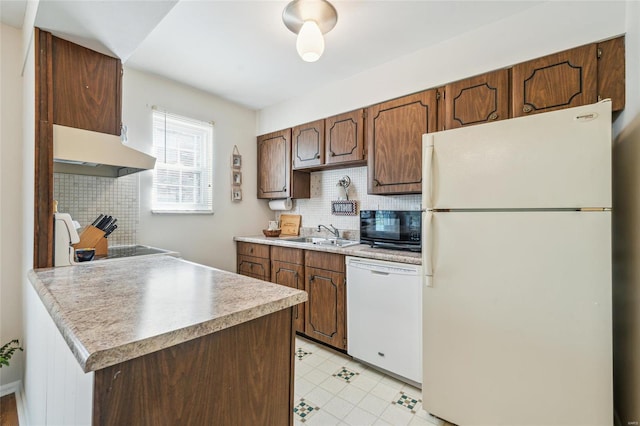 kitchen featuring tasteful backsplash, under cabinet range hood, light countertops, white appliances, and a sink