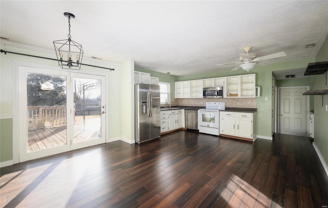 kitchen with dark wood-type flooring, appliances with stainless steel finishes, white cabinetry, dark countertops, and backsplash