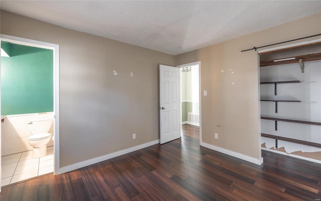 unfurnished bedroom featuring visible vents, baseboards, ensuite bath, and wood finished floors