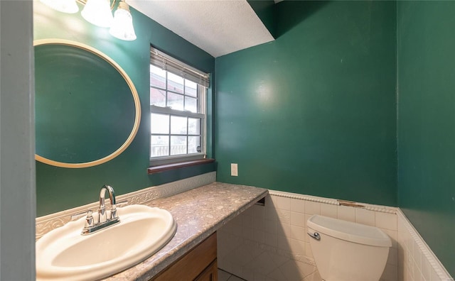 bathroom with a wainscoted wall, toilet, vanity, a textured ceiling, and tile walls