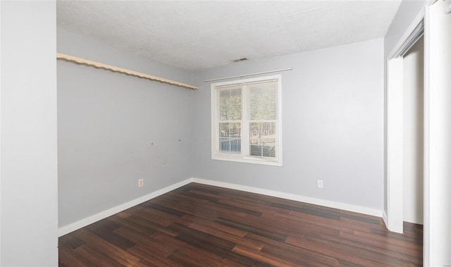 unfurnished room featuring visible vents, a textured ceiling, dark wood-type flooring, and baseboards