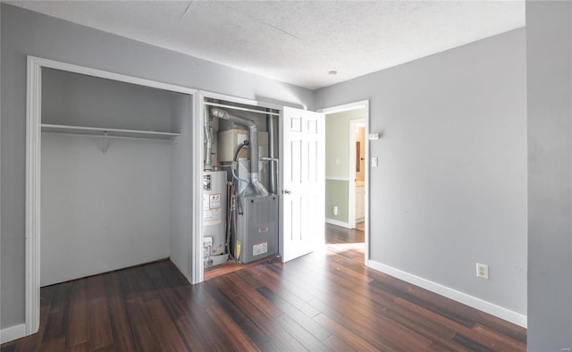 unfurnished bedroom featuring wood finished floors, baseboards, a closet, a textured ceiling, and gas water heater