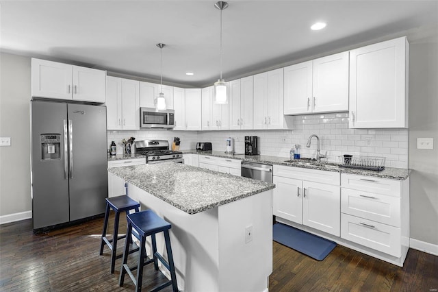 kitchen featuring a sink, light stone counters, a kitchen island, appliances with stainless steel finishes, and white cabinets