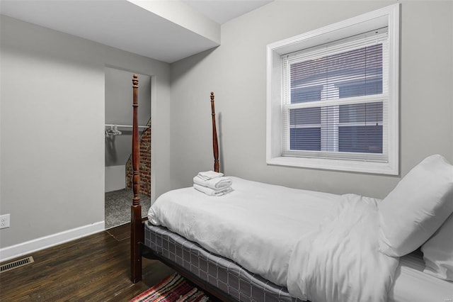 bedroom featuring a spacious closet, visible vents, baseboards, and wood finished floors