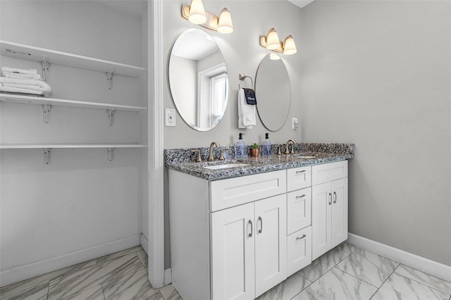 bathroom featuring double vanity, marble finish floor, baseboards, and a sink