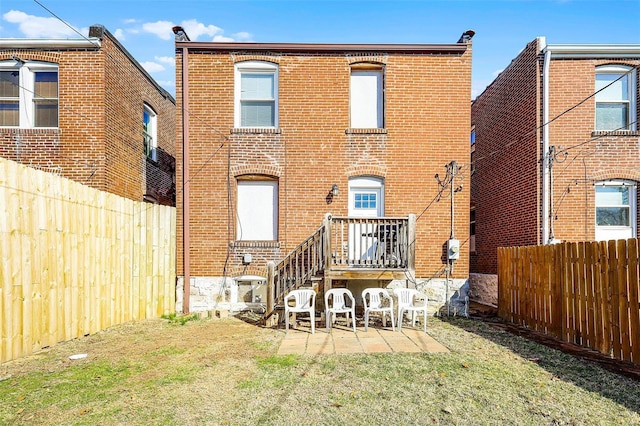 rear view of property featuring brick siding, a fenced backyard, a yard, and a patio