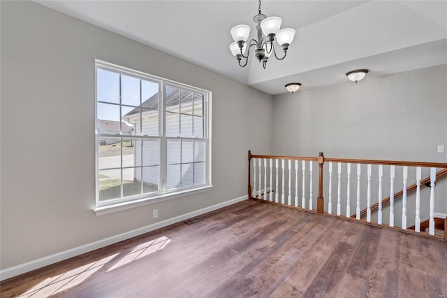 empty room with a chandelier, baseboards, and wood finished floors