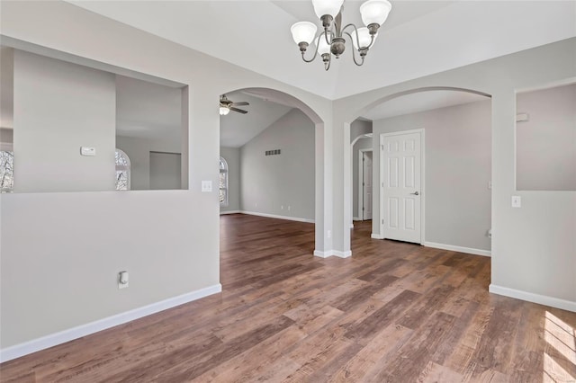 spare room featuring arched walkways, ceiling fan with notable chandelier, baseboards, and wood finished floors