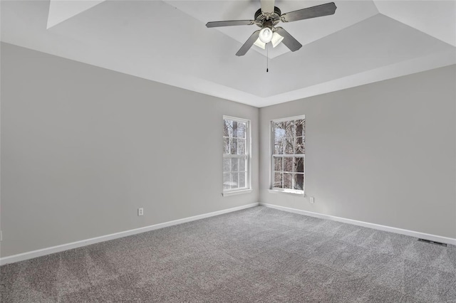 carpeted spare room featuring a tray ceiling, visible vents, baseboards, and ceiling fan