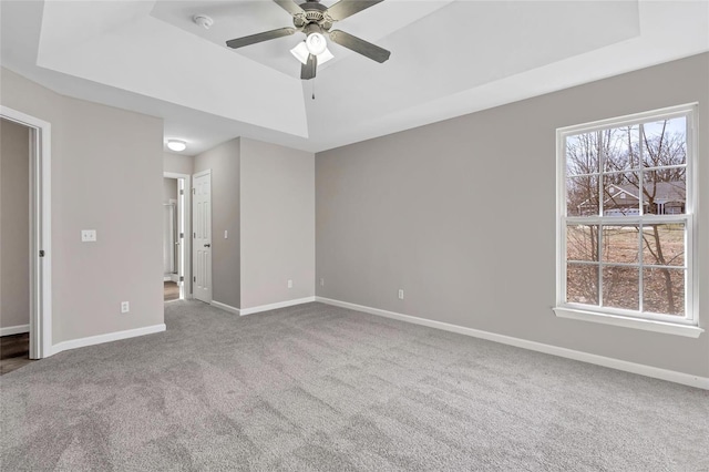 carpeted spare room with a wealth of natural light, baseboards, and a raised ceiling