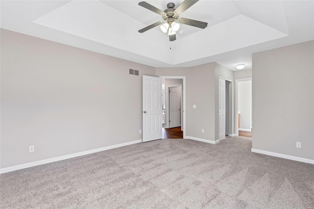 unfurnished bedroom with a ceiling fan, visible vents, baseboards, carpet floors, and a tray ceiling