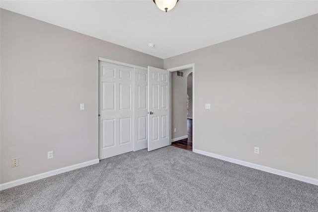 unfurnished bedroom featuring visible vents, baseboards, a closet, carpet flooring, and arched walkways