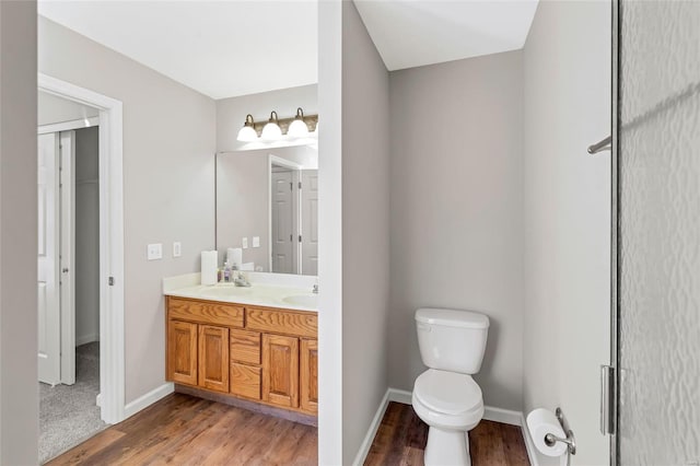 bathroom with double vanity, toilet, wood finished floors, and baseboards