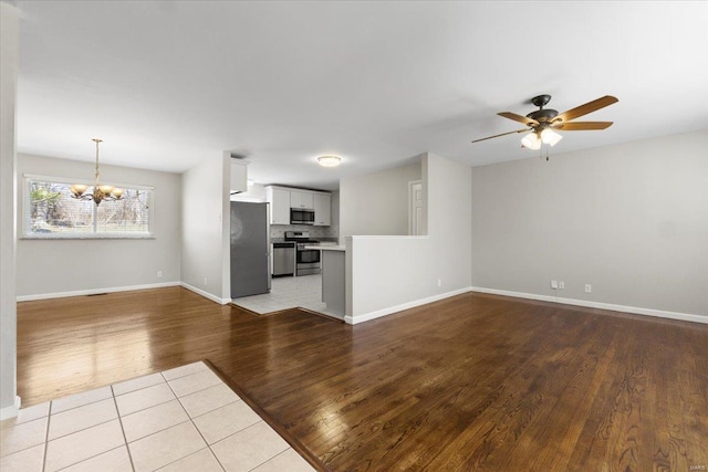 unfurnished living room featuring baseboards, wood finished floors, and ceiling fan with notable chandelier