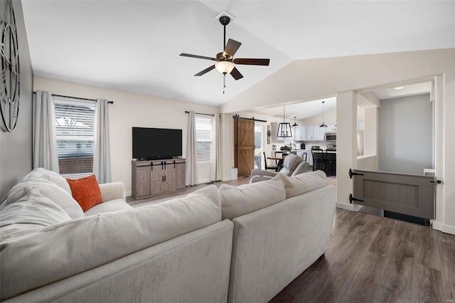 living area with dark wood-type flooring, ceiling fan, baseboards, a barn door, and lofted ceiling