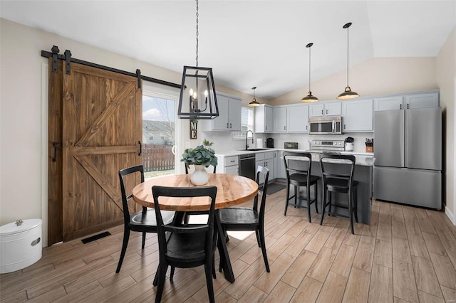 dining area featuring a barn door, visible vents, lofted ceiling, and light wood-style floors