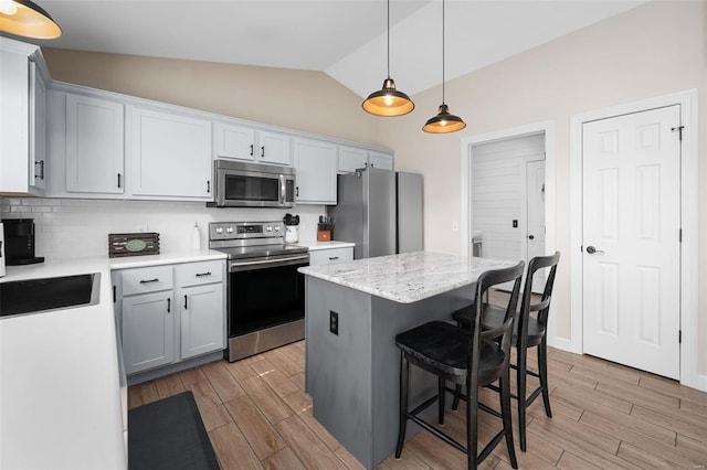 kitchen featuring wood finish floors, a kitchen island, backsplash, stainless steel appliances, and a breakfast bar area