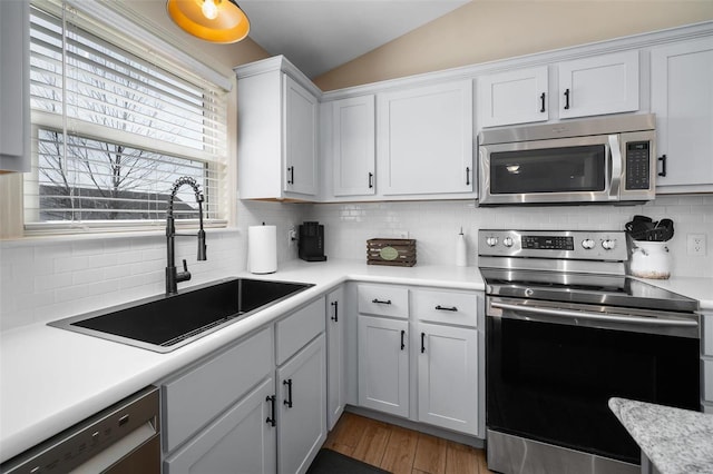 kitchen featuring light countertops, lofted ceiling, decorative backsplash, stainless steel appliances, and a sink