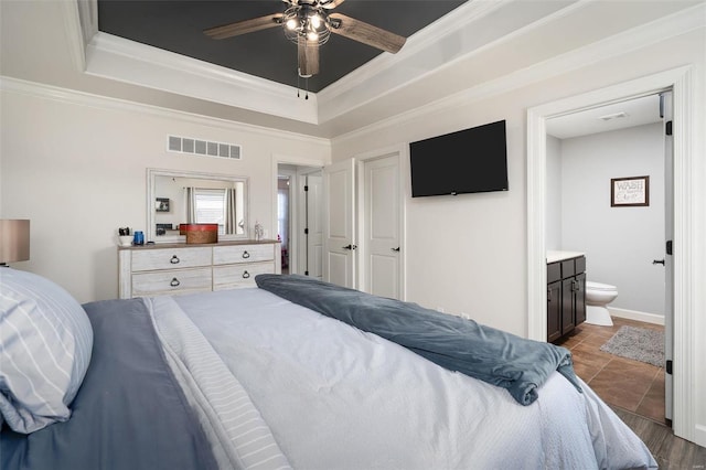 bedroom featuring a tray ceiling, visible vents, connected bathroom, and crown molding