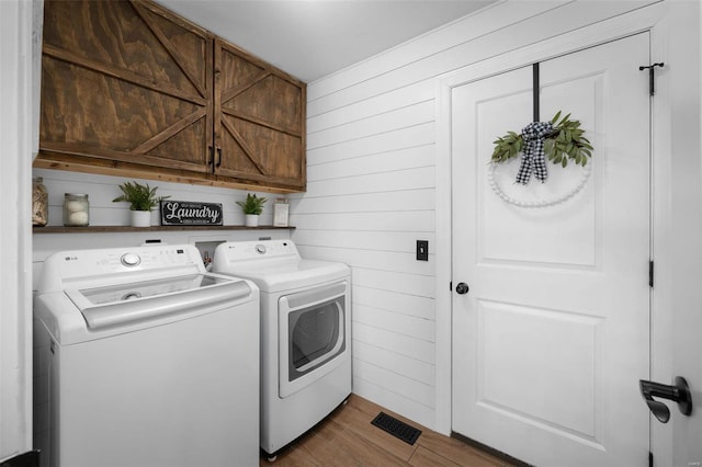 laundry area featuring cabinet space, washer and dryer, wood walls, and wood finished floors