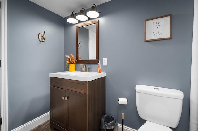 bathroom featuring baseboards, toilet, wood finished floors, and vanity