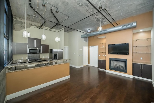 kitchen featuring dark wood-style floors, stone countertops, stainless steel appliances, a towering ceiling, and decorative light fixtures