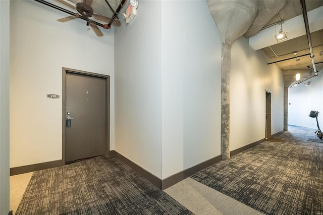 corridor with carpet flooring, baseboards, and a towering ceiling