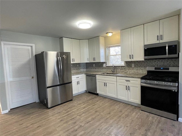 kitchen featuring light wood-type flooring, a sink, tasteful backsplash, white cabinetry, and appliances with stainless steel finishes