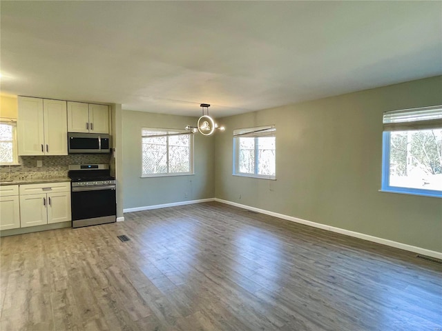 kitchen with wood finished floors, appliances with stainless steel finishes, white cabinetry, backsplash, and a chandelier