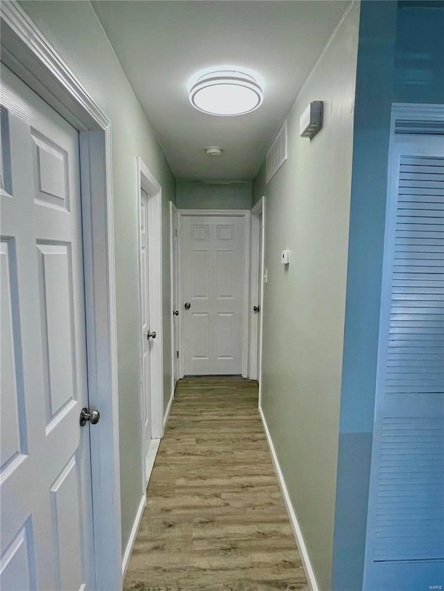 corridor with light wood finished floors, visible vents, and baseboards