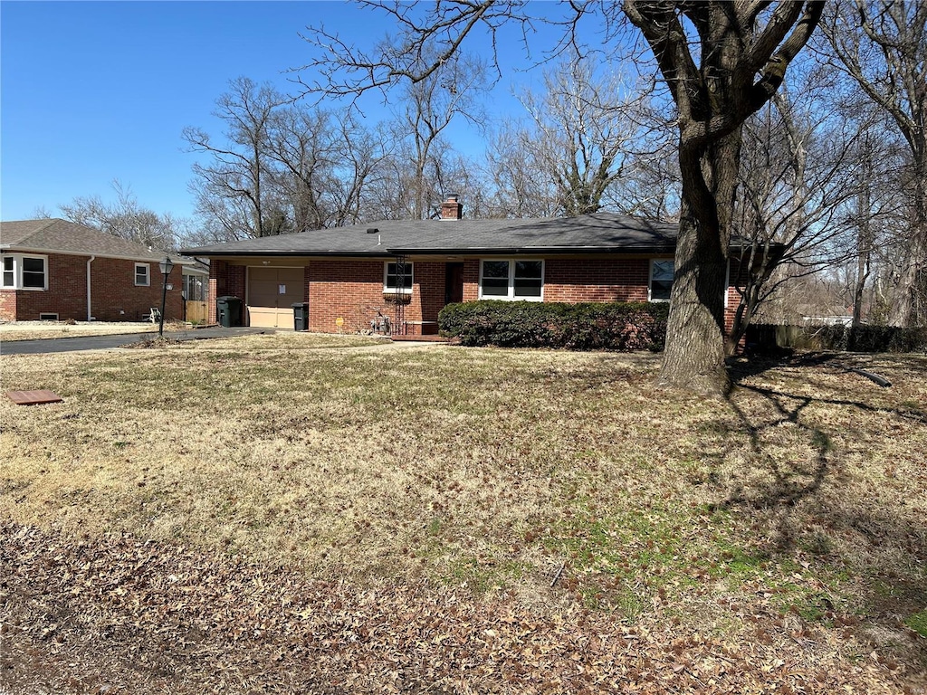 back of house with brick siding, a lawn, a chimney, a garage, and driveway