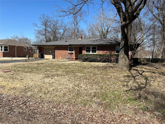 rear view of property featuring driveway, a yard, an attached garage, brick siding, and a chimney