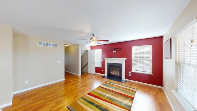 unfurnished living room with visible vents, a fireplace with flush hearth, light wood-style flooring, a ceiling fan, and baseboards