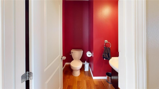 half bathroom featuring toilet, vanity, baseboards, and wood finished floors