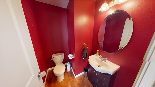 half bathroom with baseboards, toilet, wood finished floors, and vanity