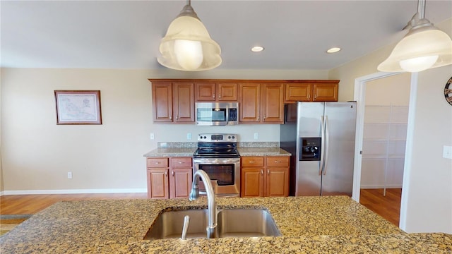 kitchen with light stone counters, pendant lighting, stainless steel appliances, and a sink