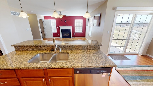 kitchen with a sink, decorative light fixtures, light stone counters, stainless steel dishwasher, and open floor plan