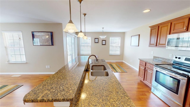 kitchen with baseboards, dark stone counters, light wood-style flooring, a sink, and appliances with stainless steel finishes