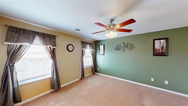 carpeted empty room with visible vents, a ceiling fan, and baseboards