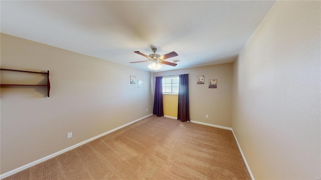 spare room featuring light colored carpet, a ceiling fan, and baseboards