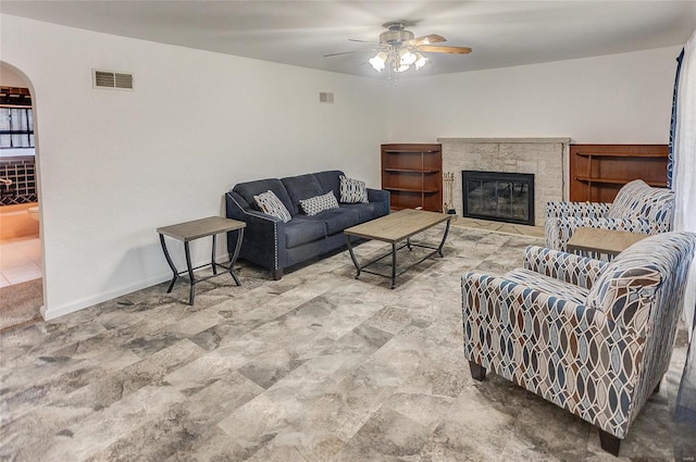 living room with visible vents, arched walkways, a fireplace, baseboards, and ceiling fan