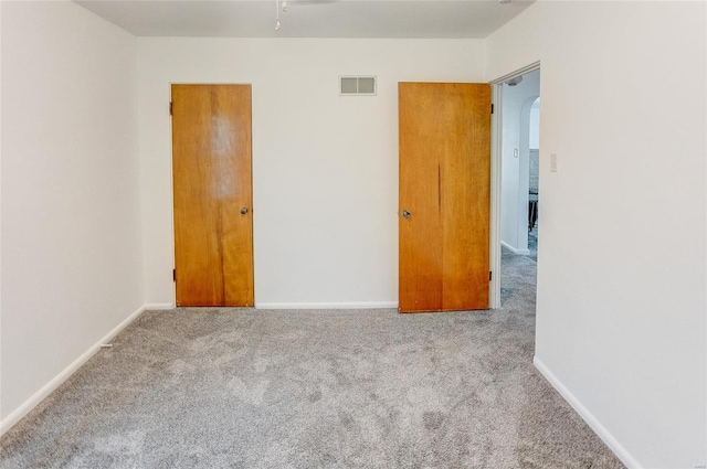 carpeted spare room with baseboards, visible vents, and arched walkways