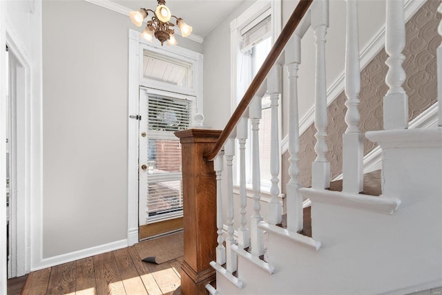 foyer with wood finished floors, baseboards, ornamental molding, stairs, and a notable chandelier