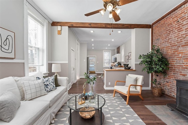 living area featuring beam ceiling, a wood stove, wood finished floors, and a healthy amount of sunlight