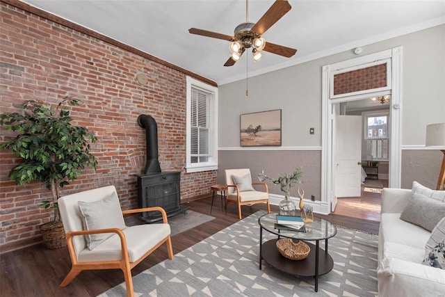 living area featuring ornamental molding, brick wall, a wood stove, and wood finished floors