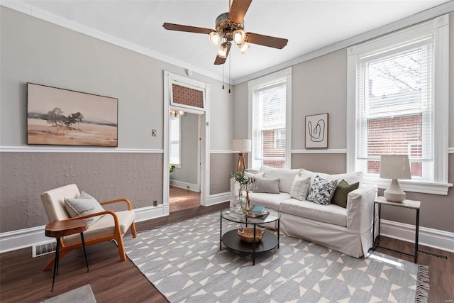 living area with a ceiling fan, wood finished floors, visible vents, baseboards, and crown molding