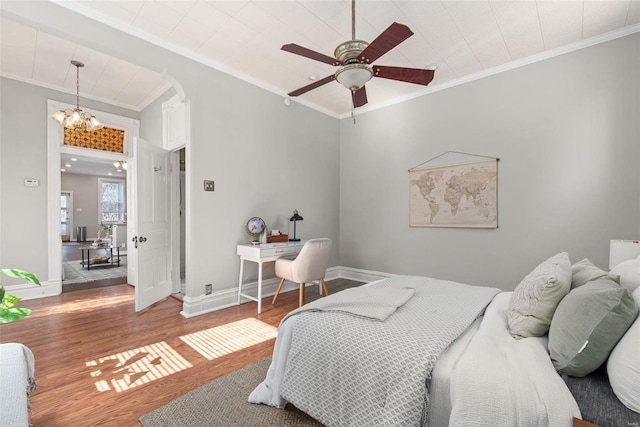 bedroom with arched walkways, crown molding, baseboards, and wood finished floors