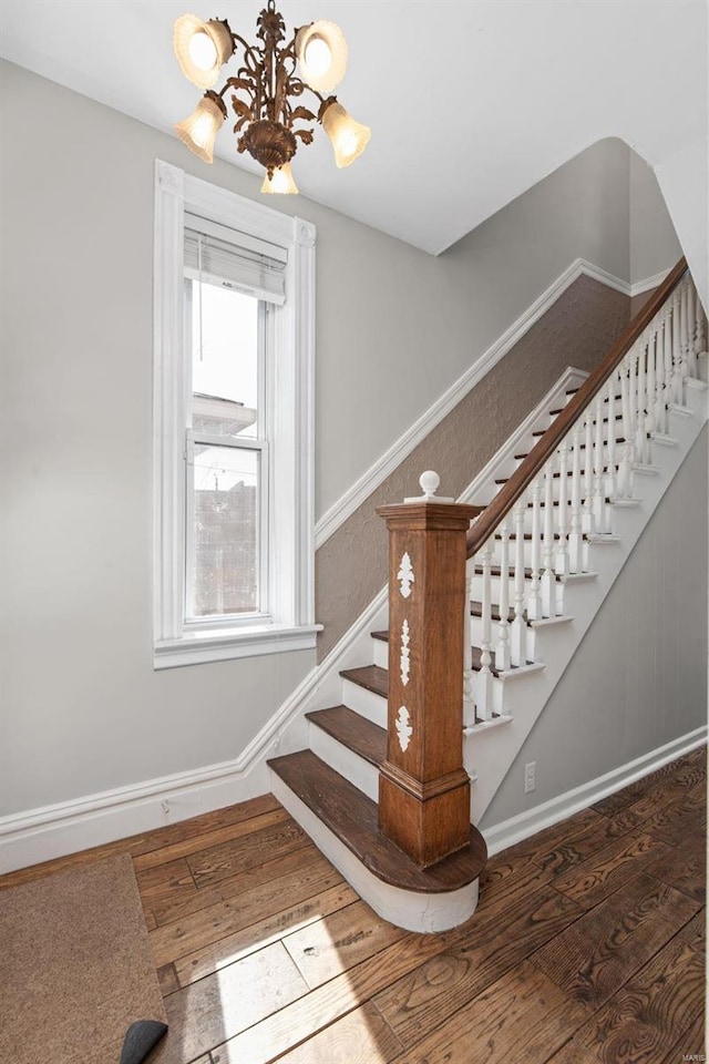 stairs featuring baseboards, an inviting chandelier, and wood-type flooring