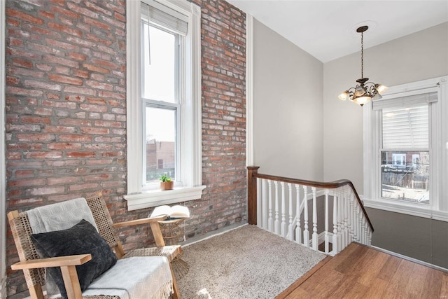 living area featuring an upstairs landing, brick wall, an inviting chandelier, and wood finished floors