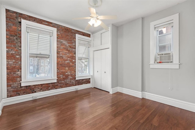 empty room with brick wall, a ceiling fan, baseboards, and wood finished floors